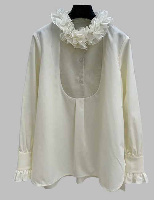 White blouse with ruffled collar on a hanger against a light background